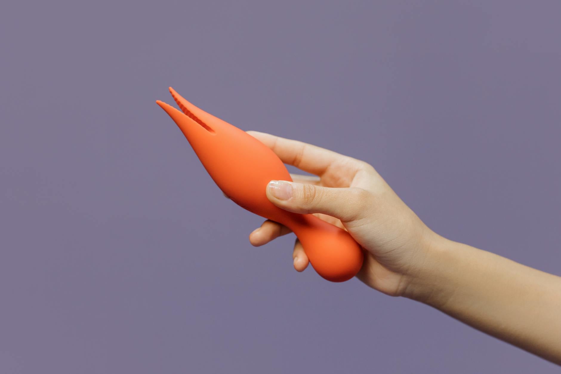 Una mano sosteniendo un vibrador naranja moderno contra un fondo minimalista, mostrando sexualidad contemporánea