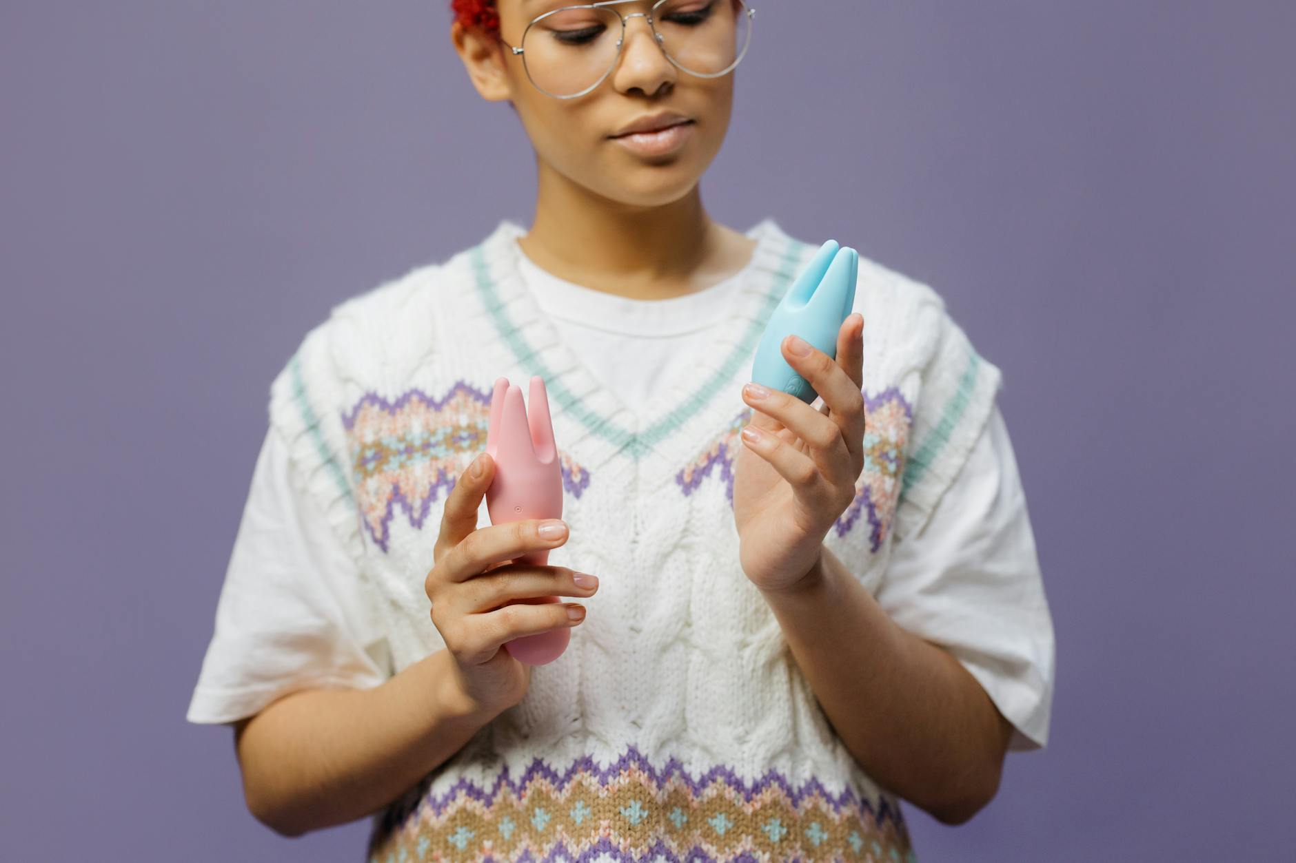 Woman with eyeglasses thoughtfully holding vibrators, representing comfort with pleasure exploration