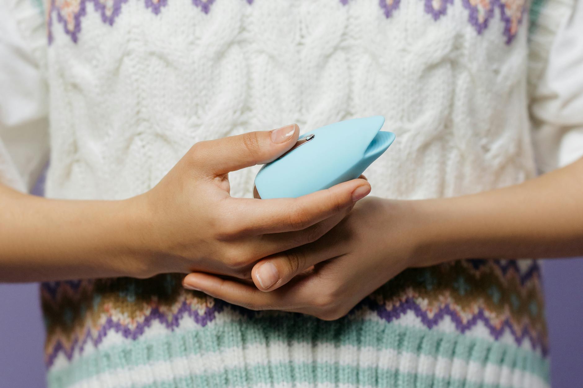 Close-up of hands holding a blue personal massager, emphasizing intimate connection and comfort.