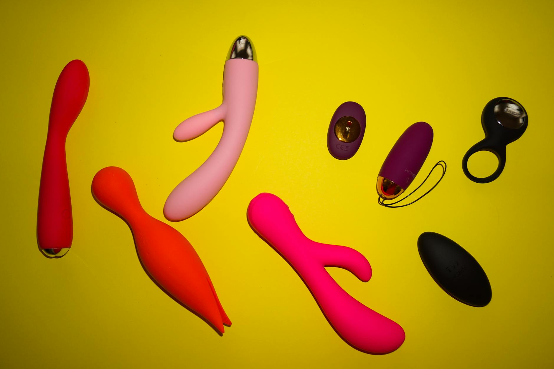Vibradores de colores brillantes dispuestos sobre una superficie amarilla vibrante, mostrando diversidad y diseño moderno